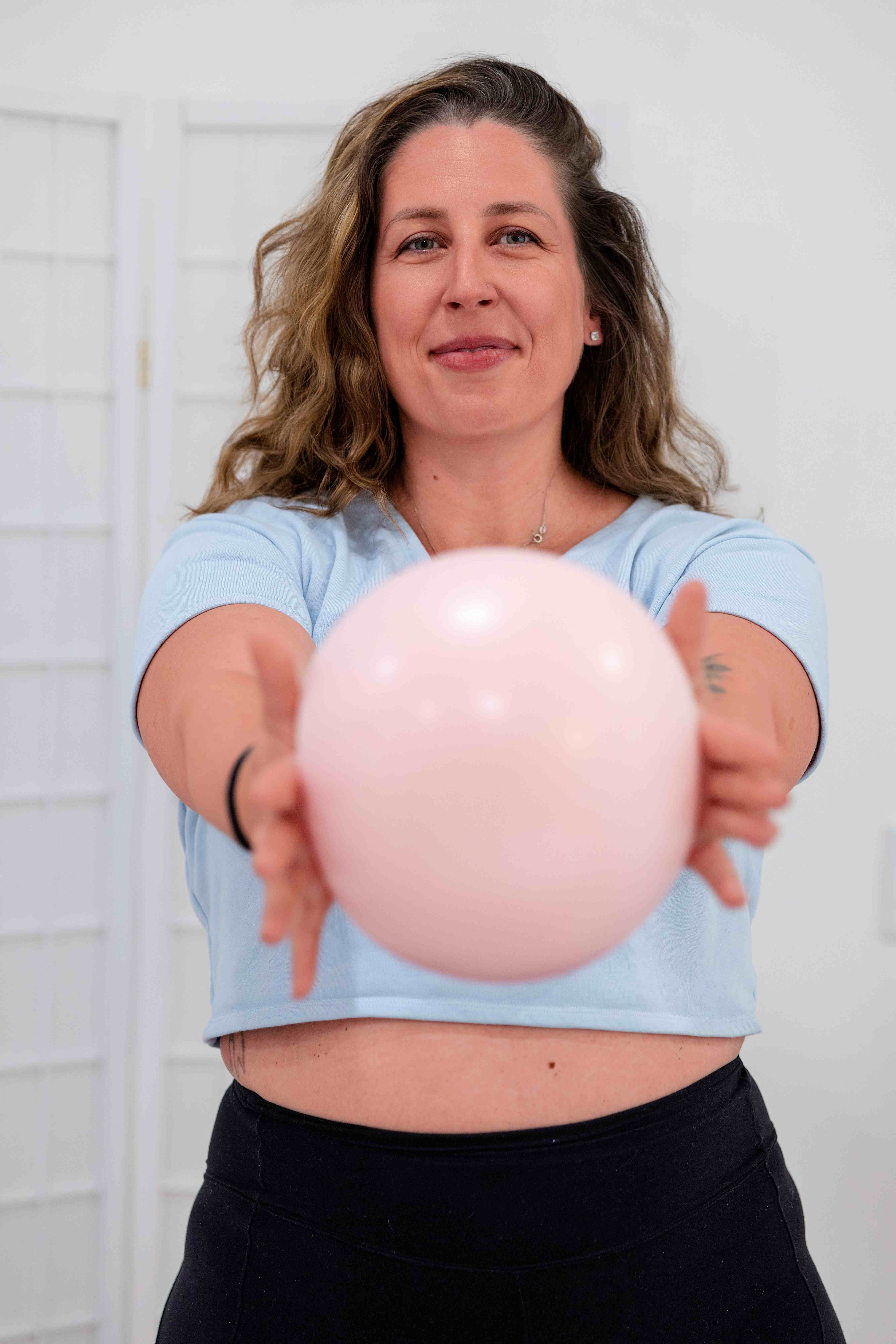 Samantha smiling and holding out a pink Pilates ball